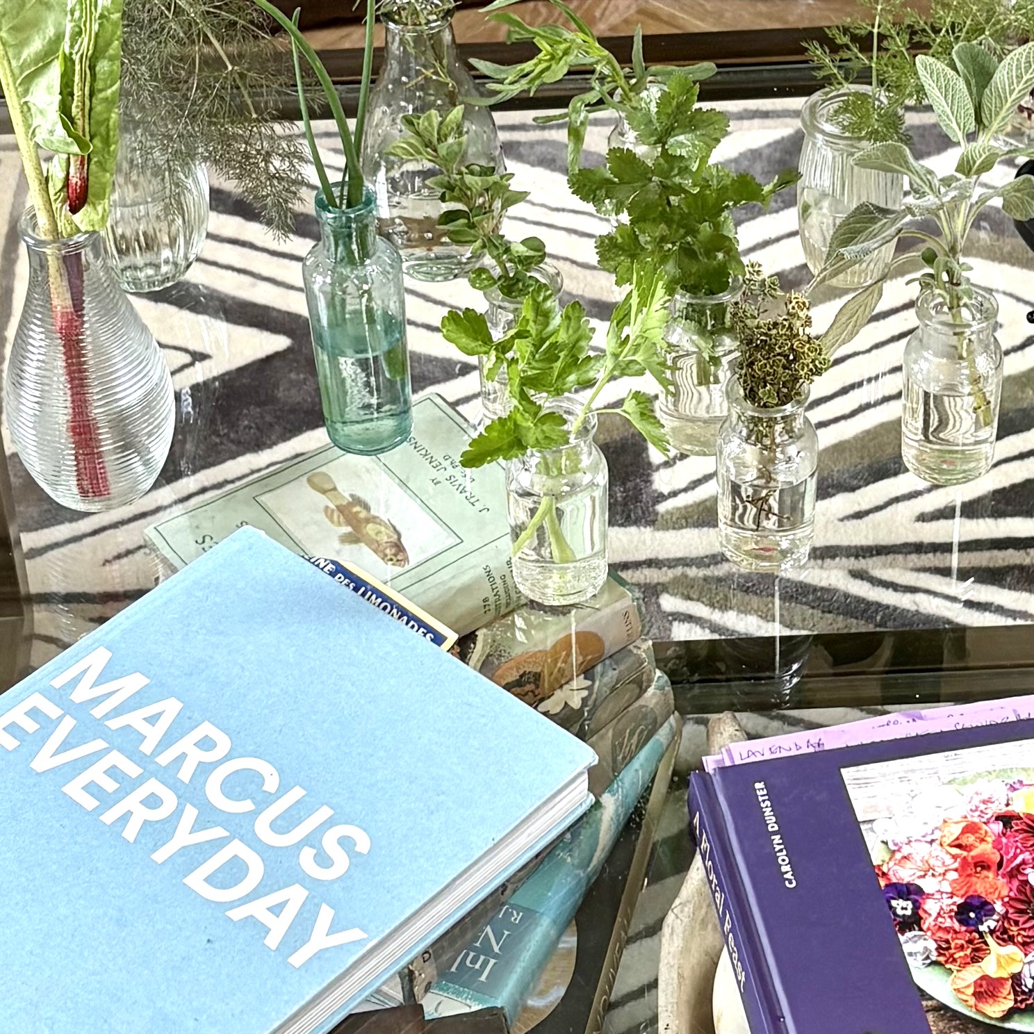 Cuttings of herbs and leaves in glass bottles on a table with gardening books